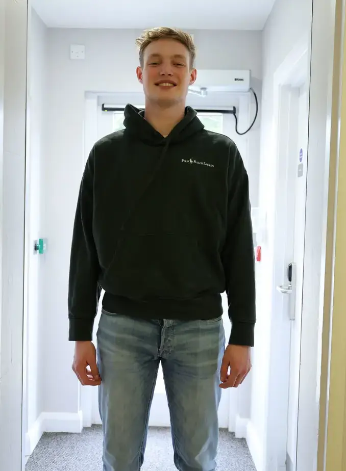 Male student wearing a black hoodie stood in corridor