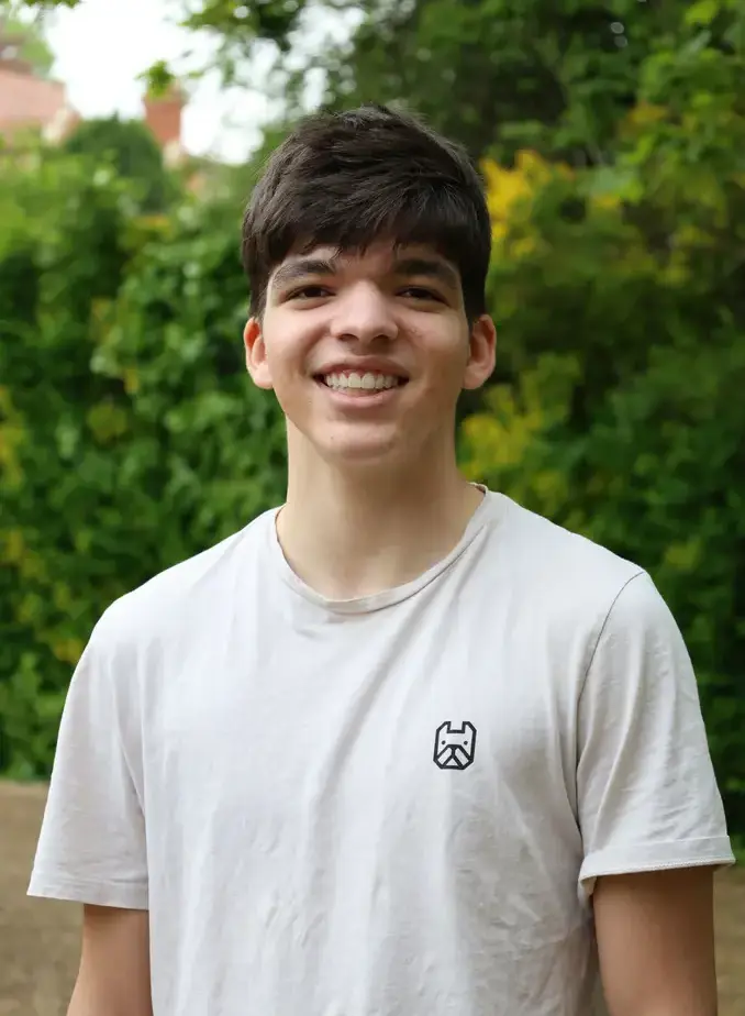 Male student wearing a white shirt with greenery in the background
