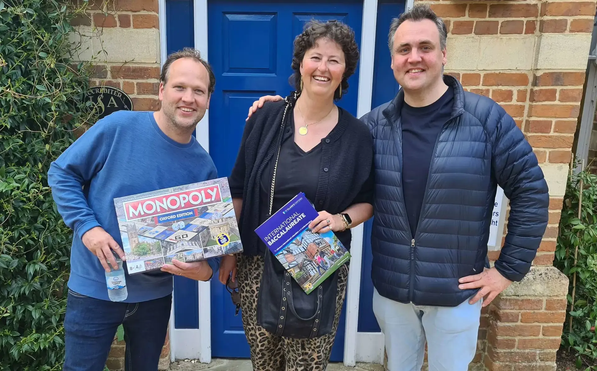 Alumni posing with Oxford edition of Monopoly and IB brochure