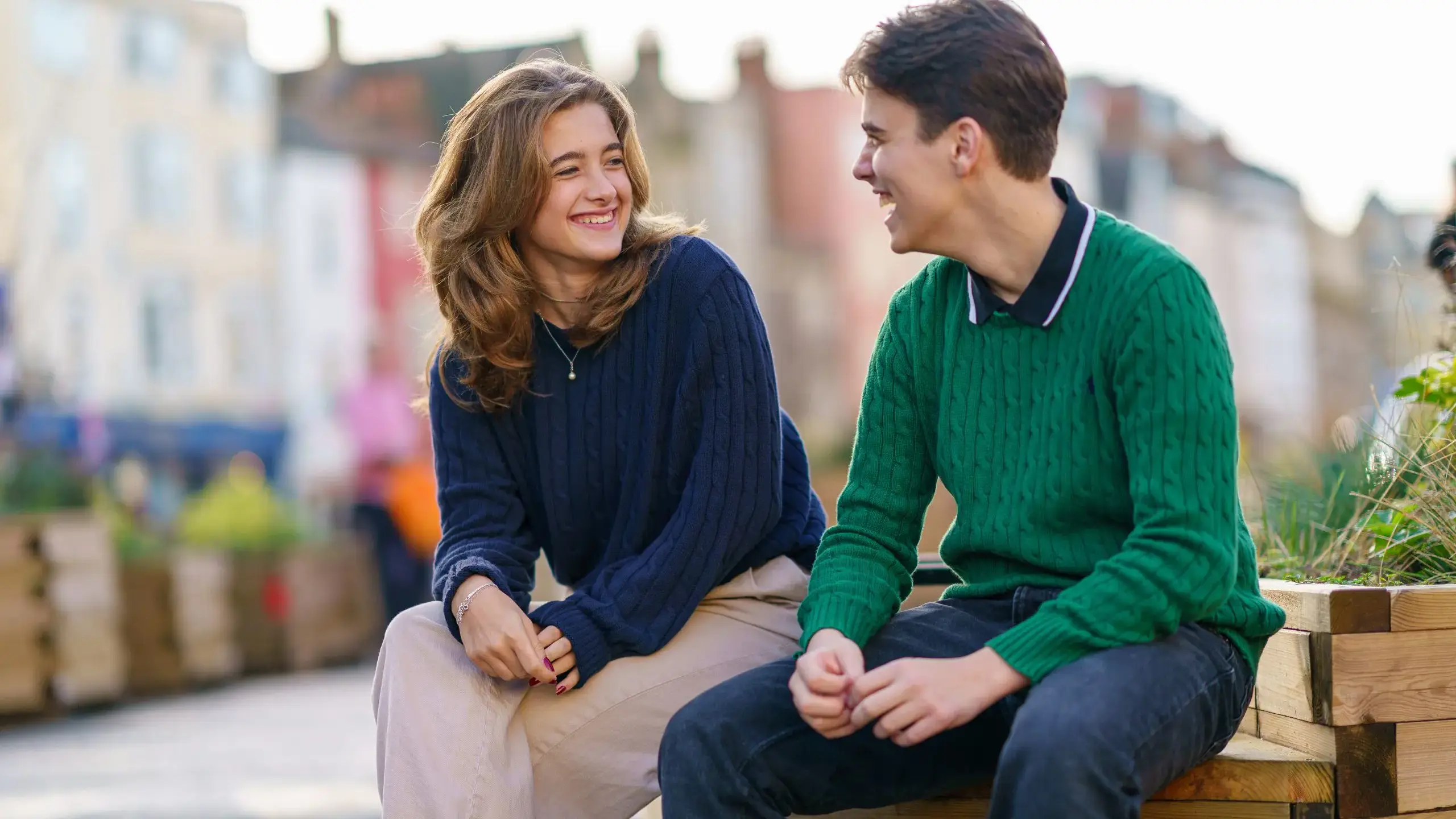 Students sitting on bench outside, smiling at each other