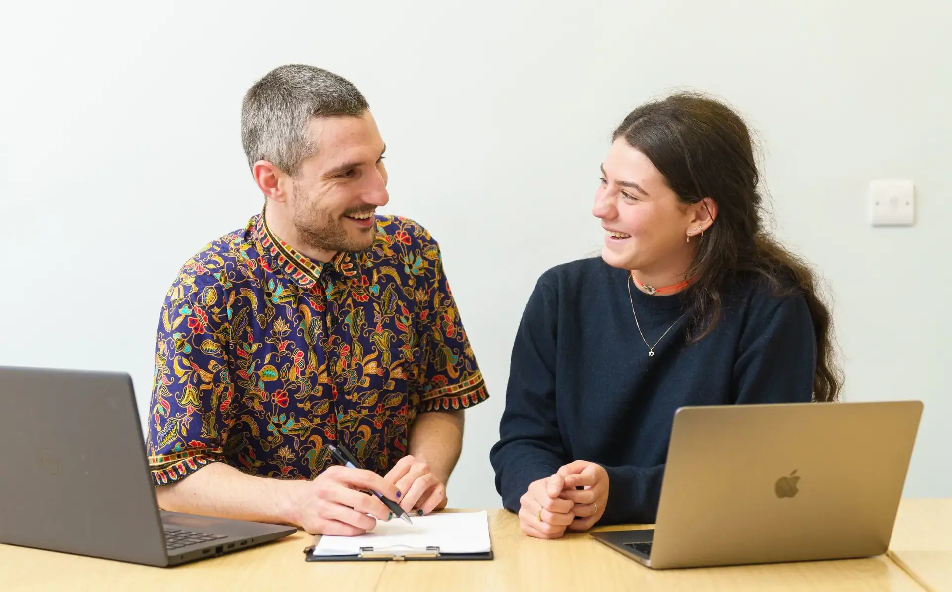 Two DELTA students chatting over the top of laptops
