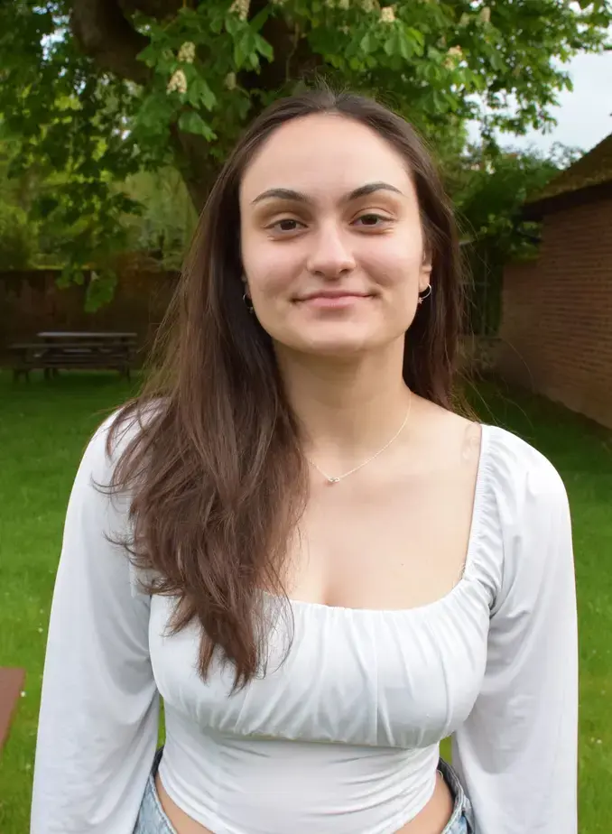Female student wearing white shirt with greenery behind her