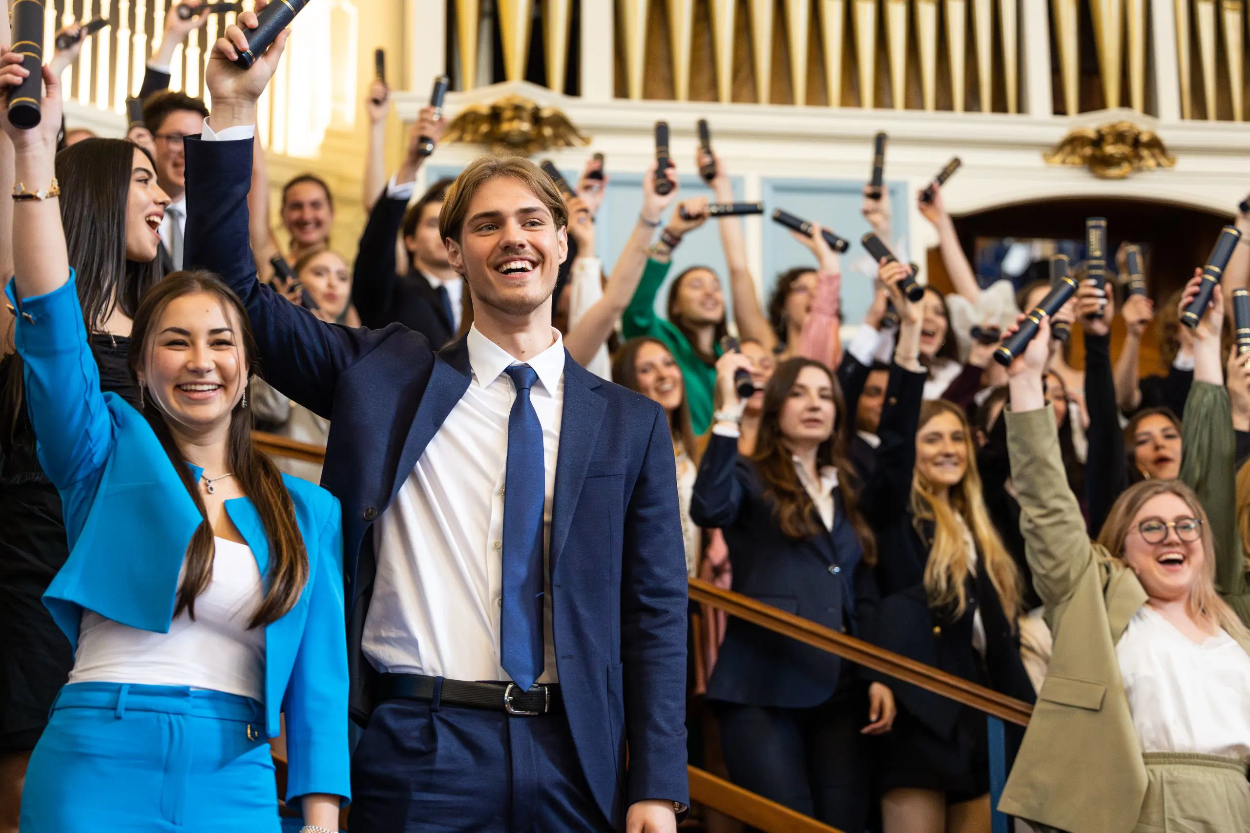 Graduating students holding diplomas and jumping in front of historic school building