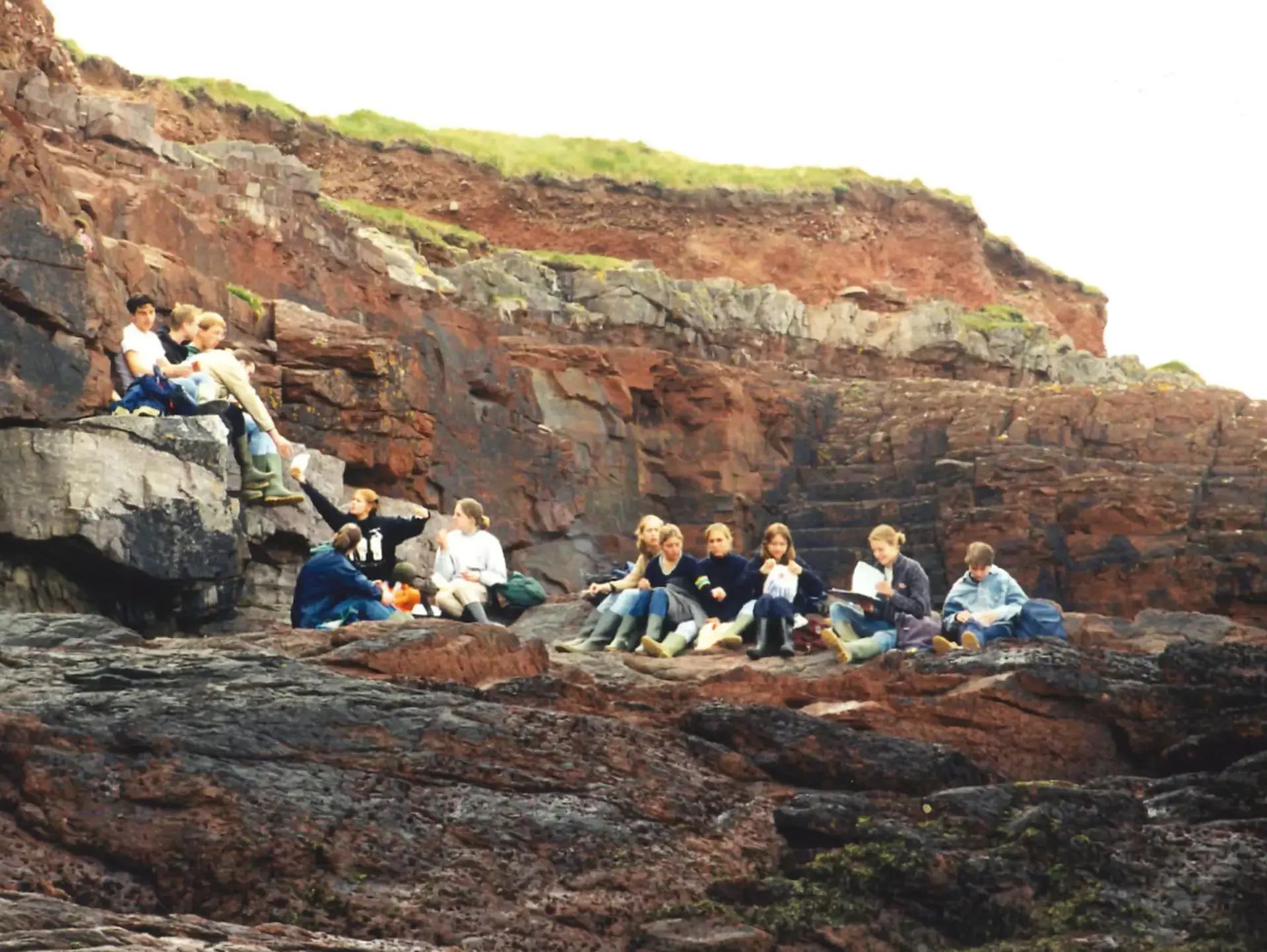 Older photograph of people sitting on grass in rolling hills
