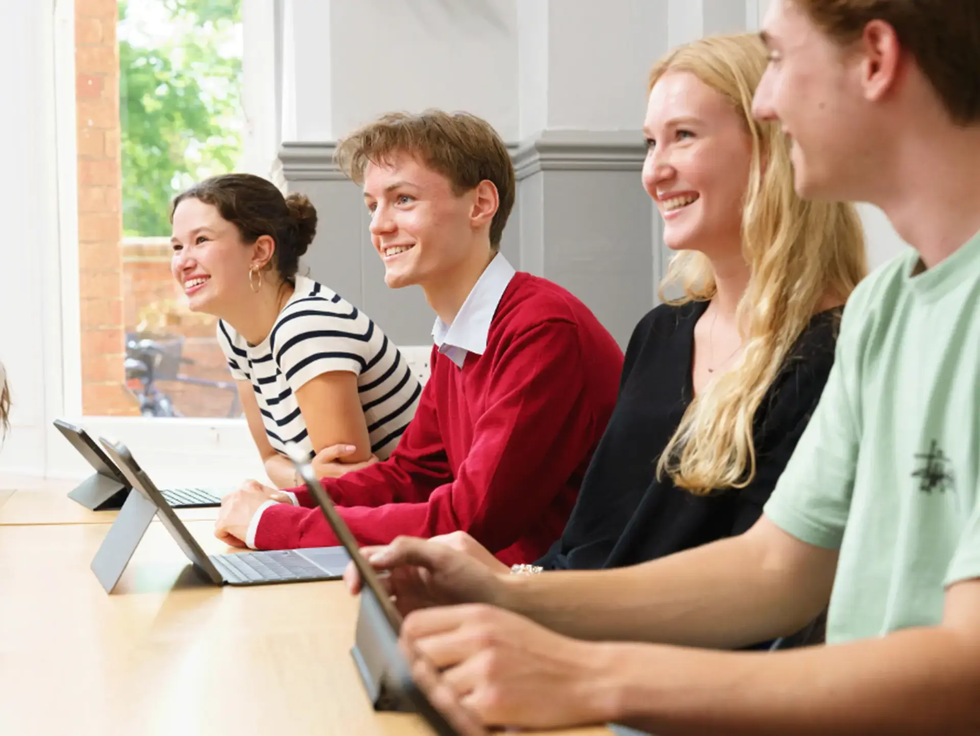 Four students sitting at desk, smiling