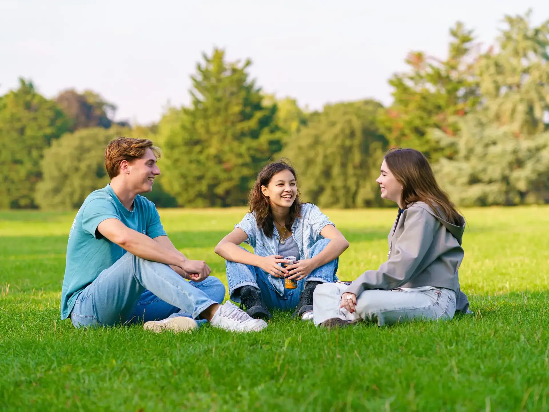 Students sat in circle in a field laughing and talking