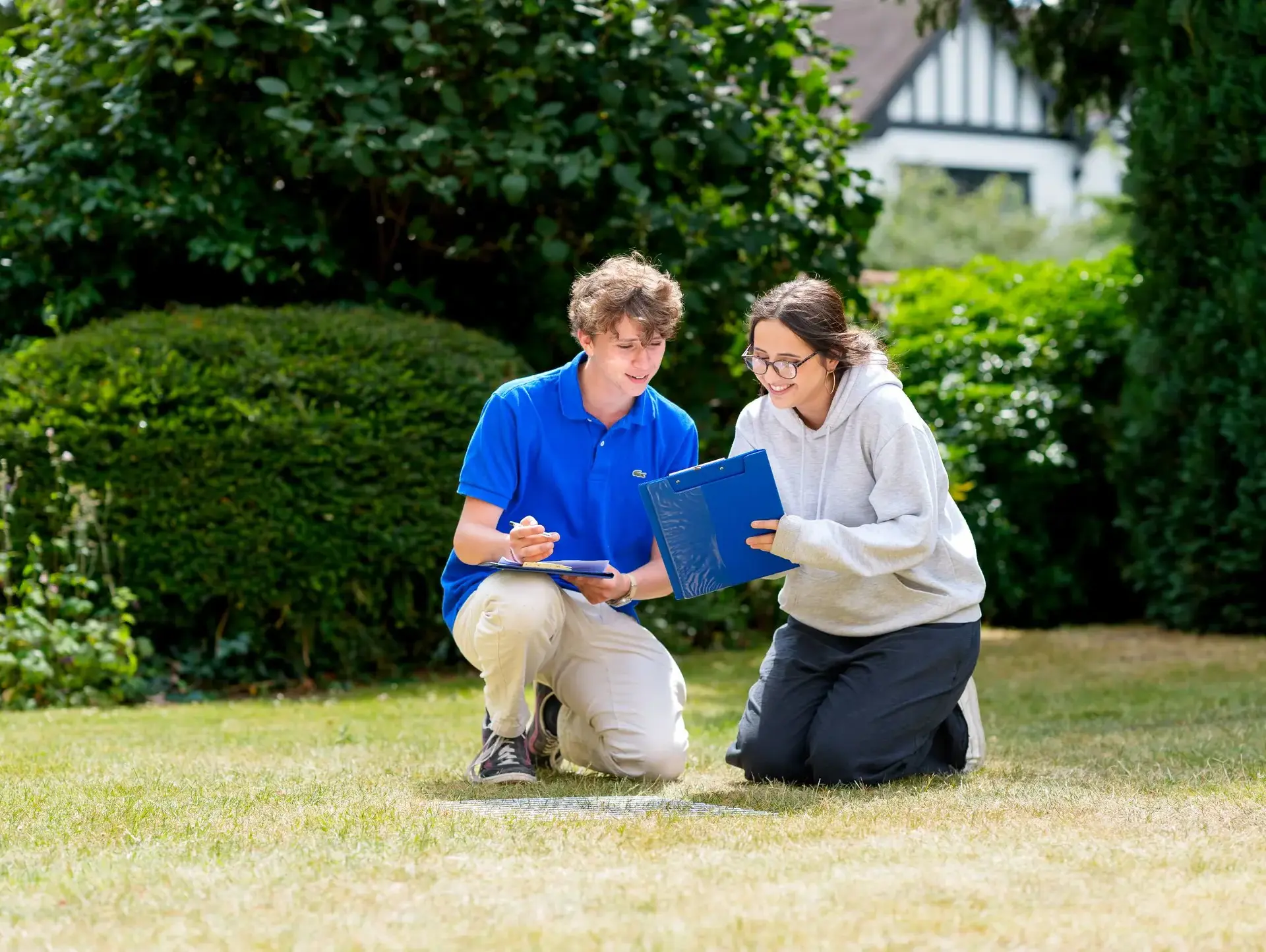 Two students kneeling down over a book outside