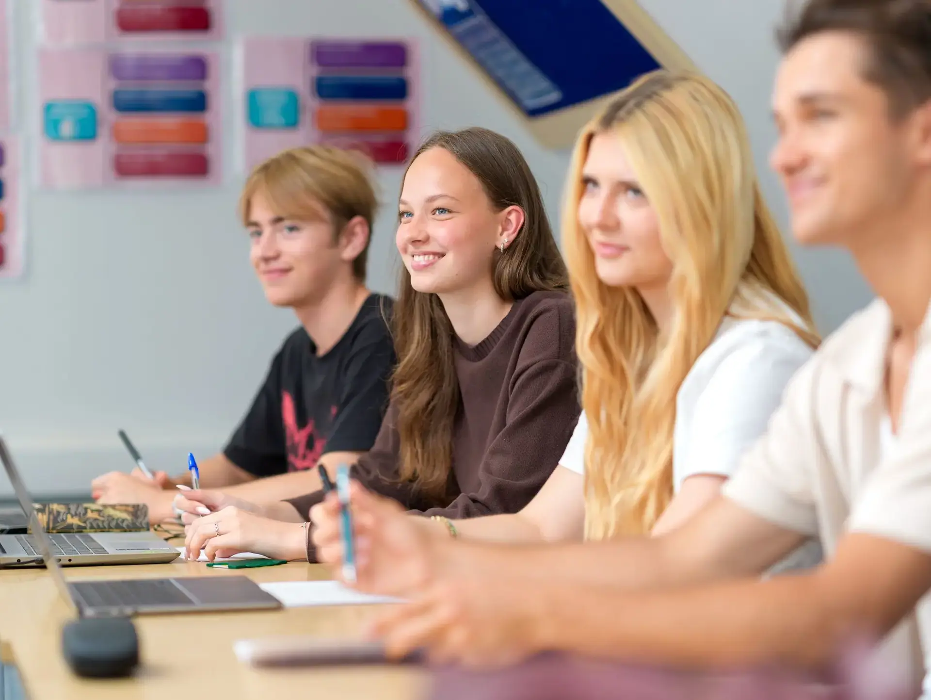 Four students sitting at desk, smiling
