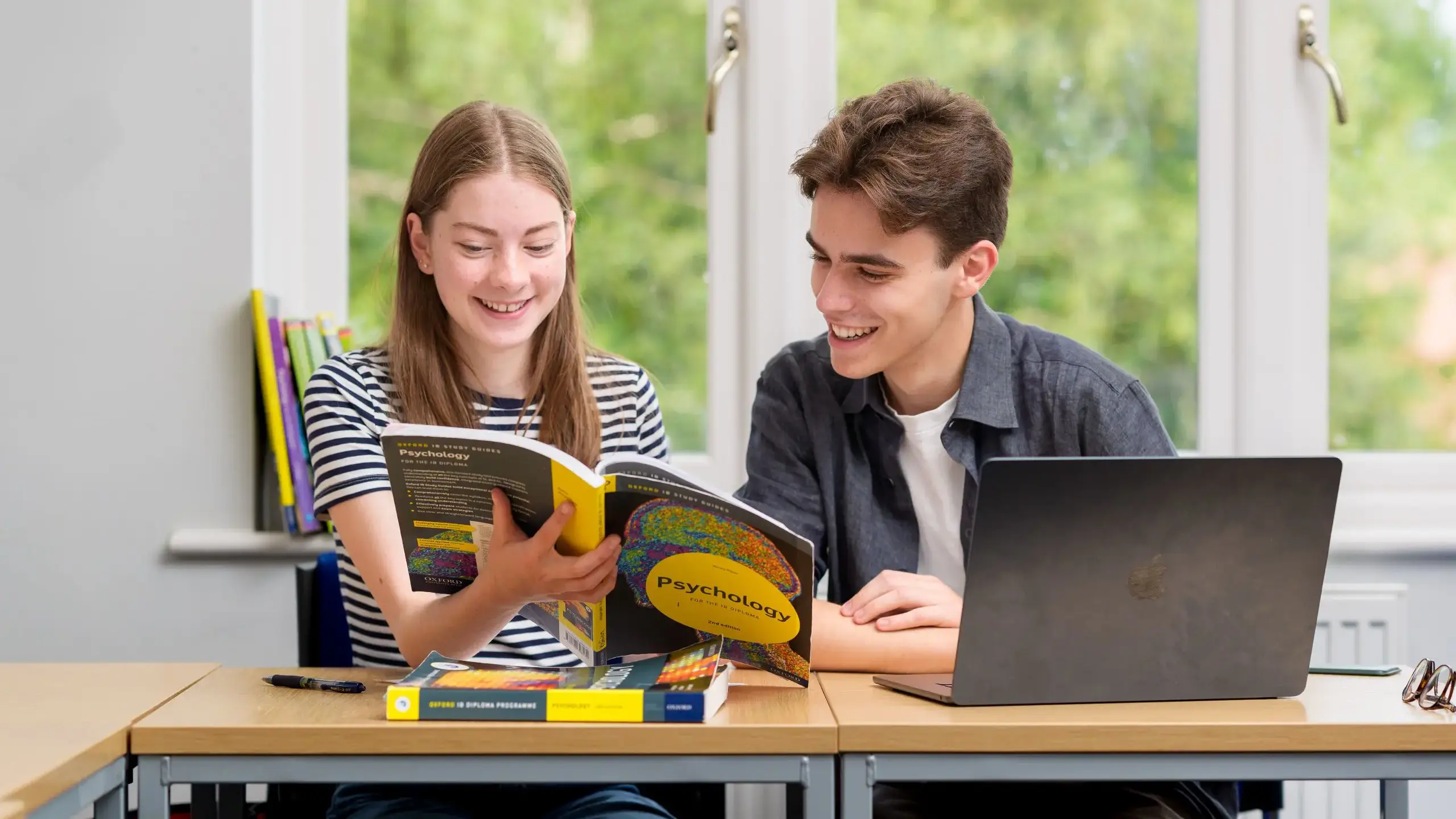 Two students smiling, looking at book