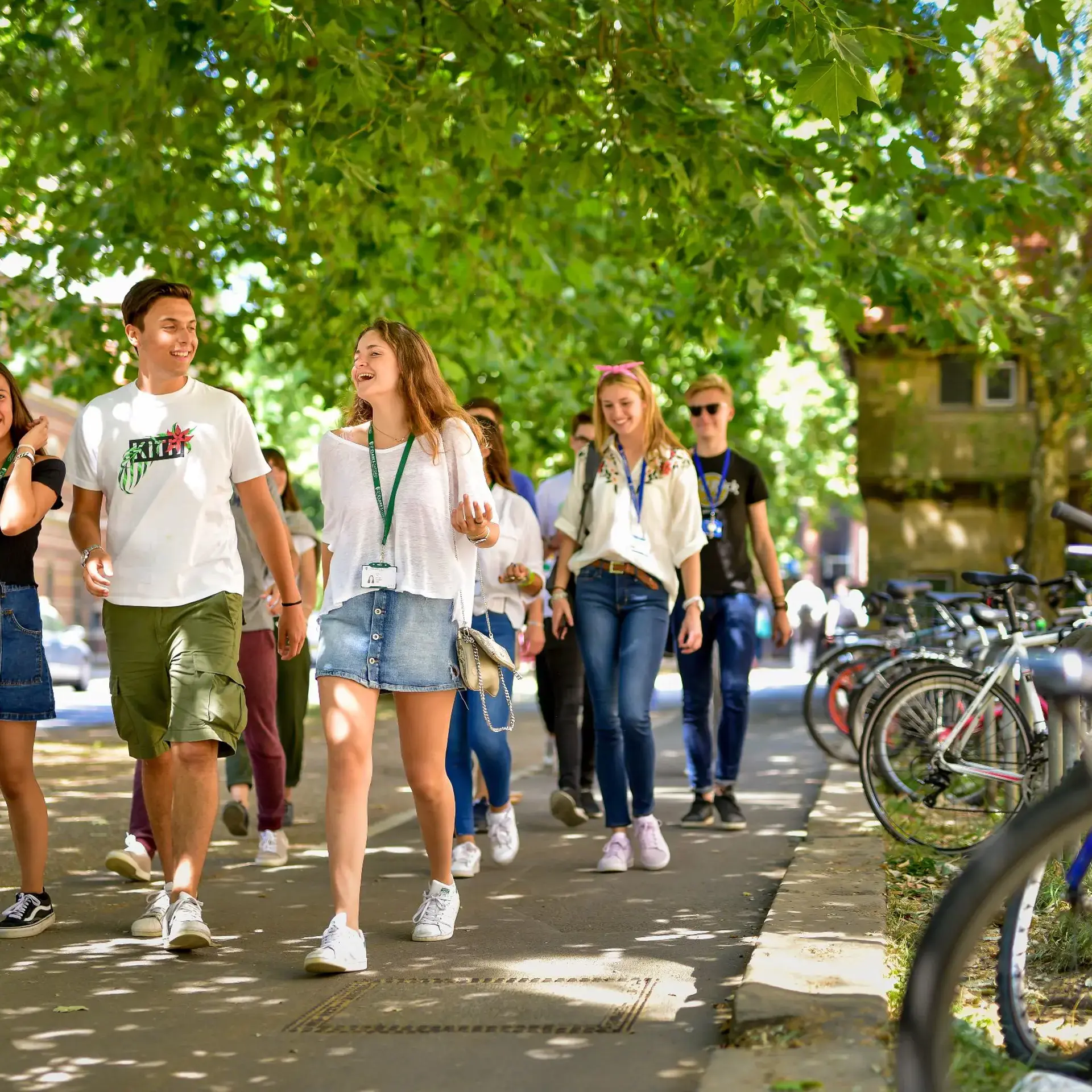 Students wearing lanyards walking down street lined with pushbikes