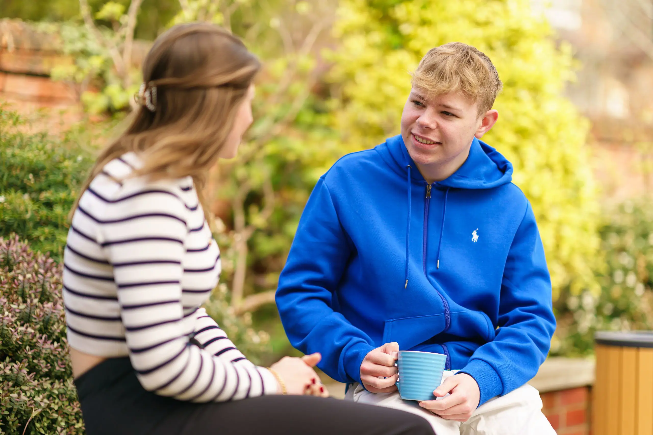 Two people chatting outside, one holding a blue mug
