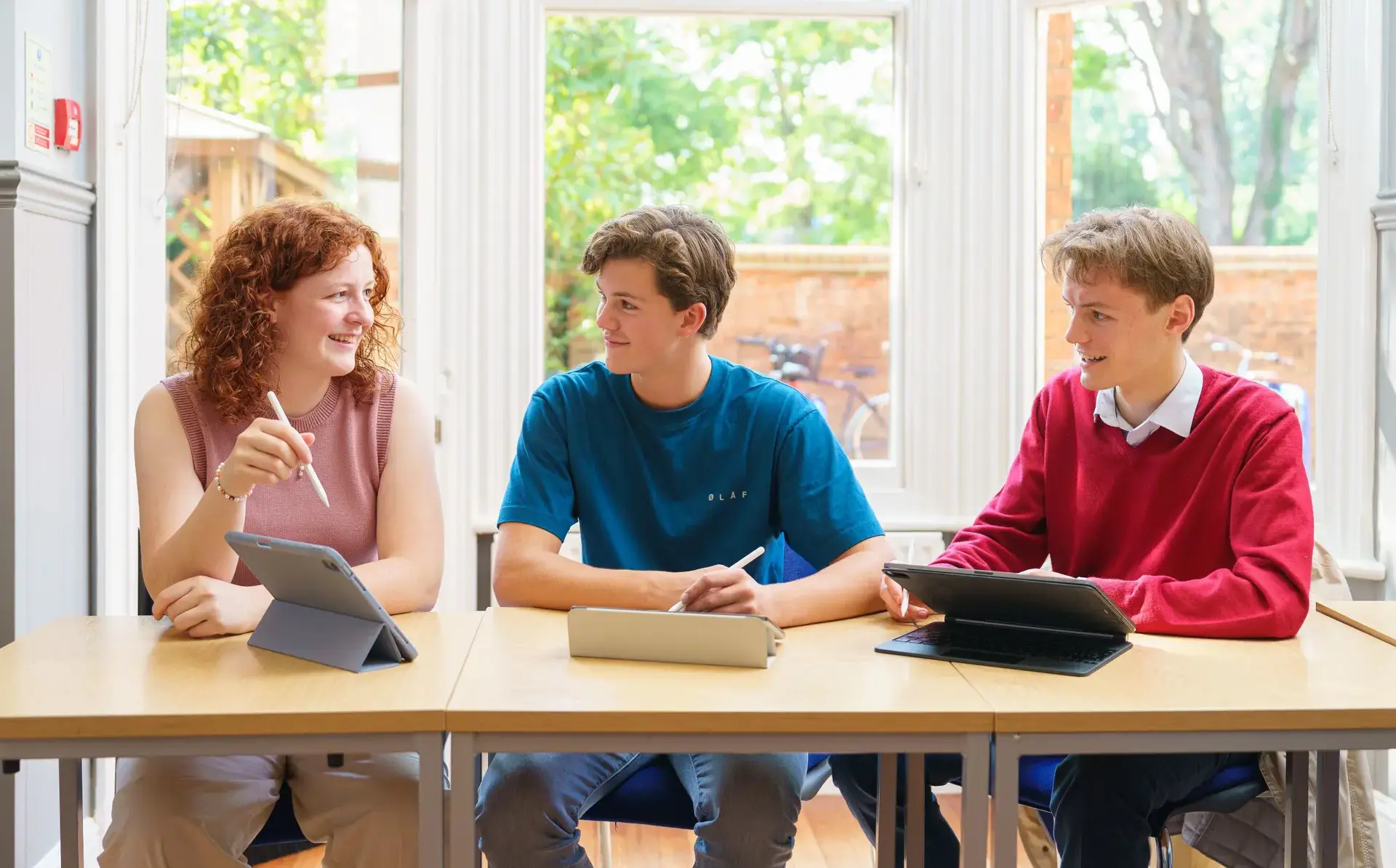 Three students working at tablets in front of window