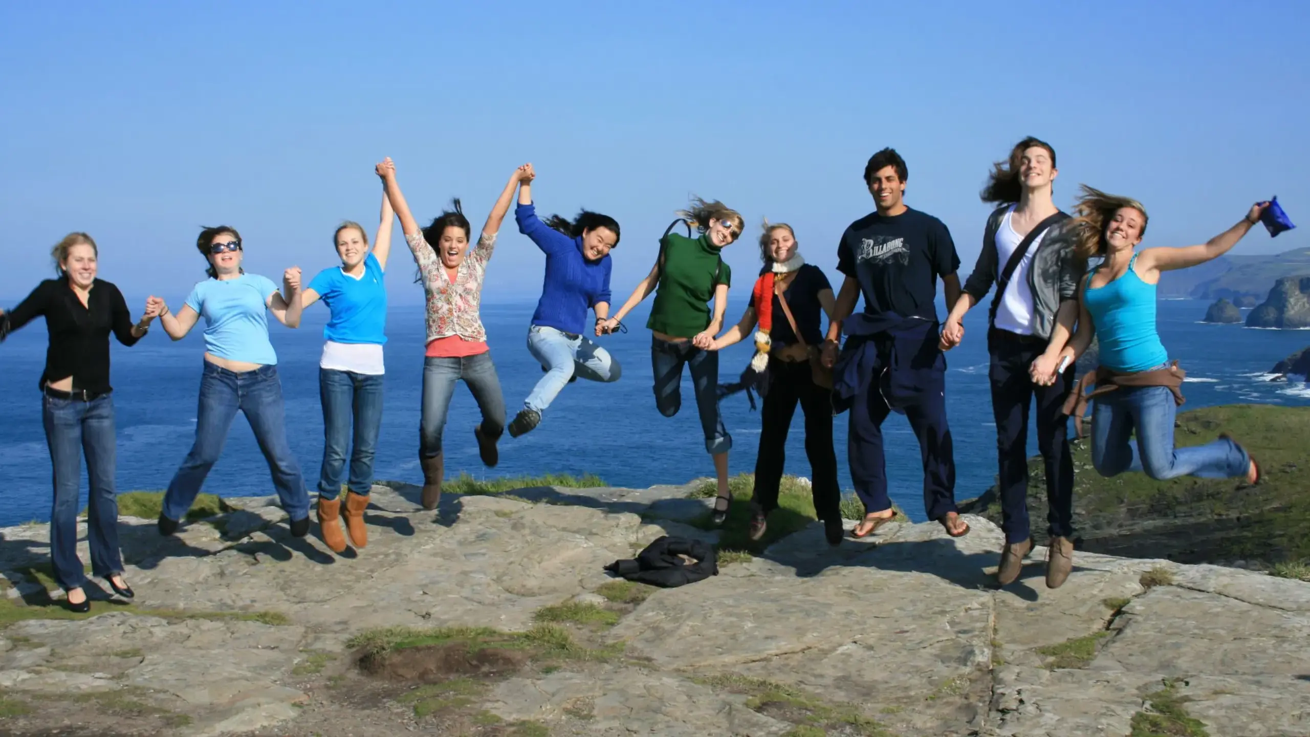 Students standing on cliff, jumping while holding hands