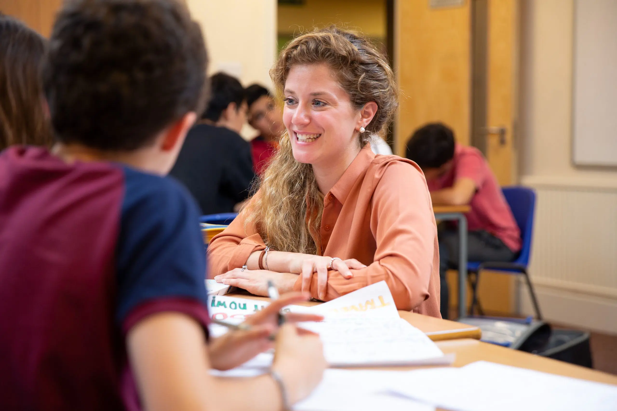 Teacher smiling, chatting with students at table