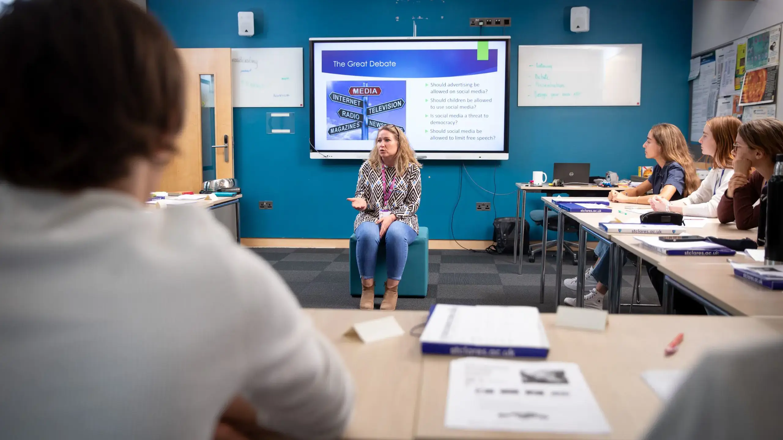 Teacher sitting on chair in middle of classroom giving lesson