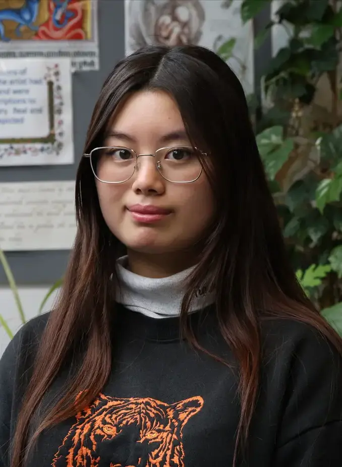 Female student wearing glasses andblack sweater with plants in the background