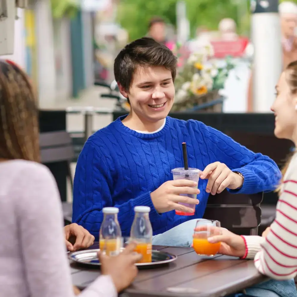 Male student drinking juice at a cafe with friends.