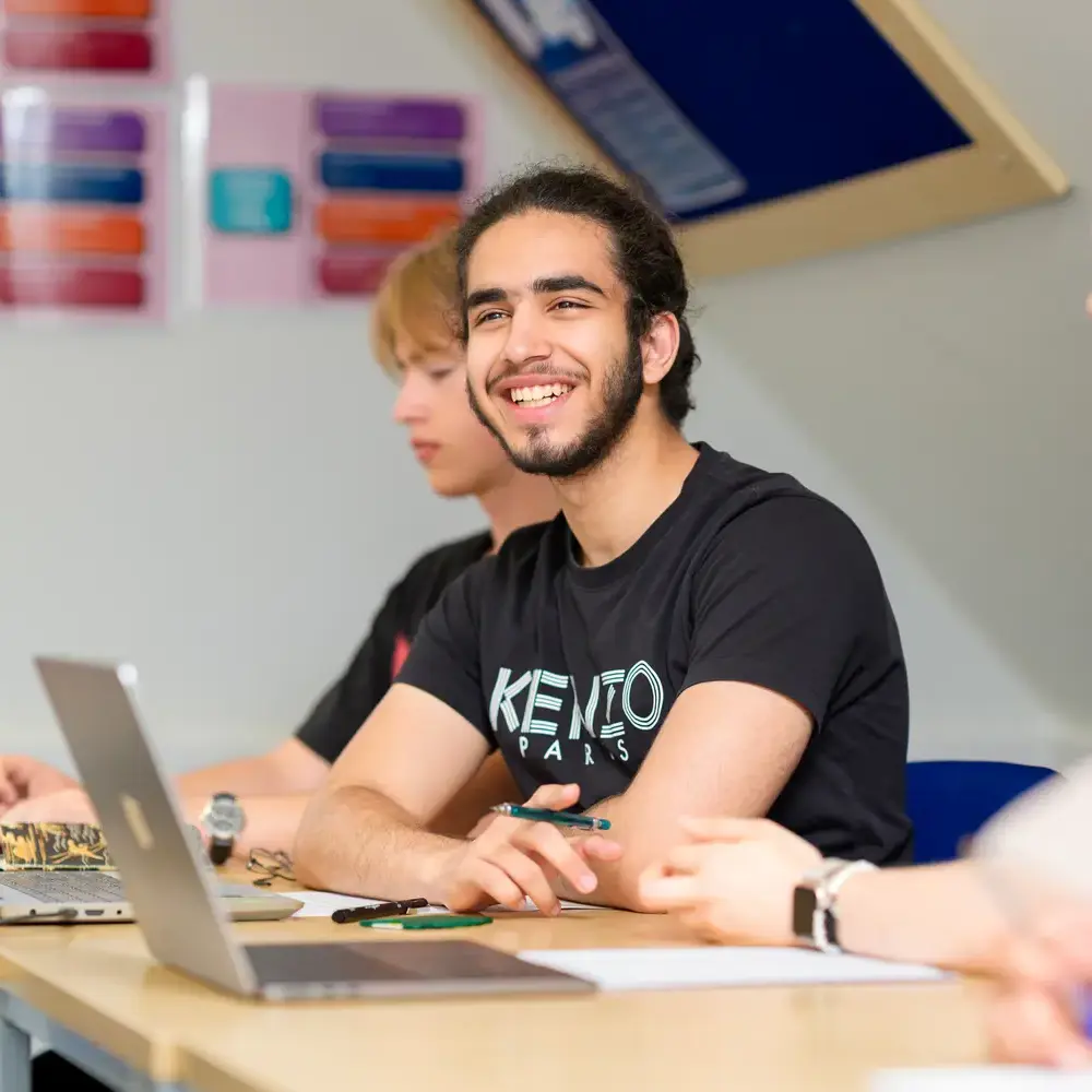 Male student sat in classroom smiling at teacher