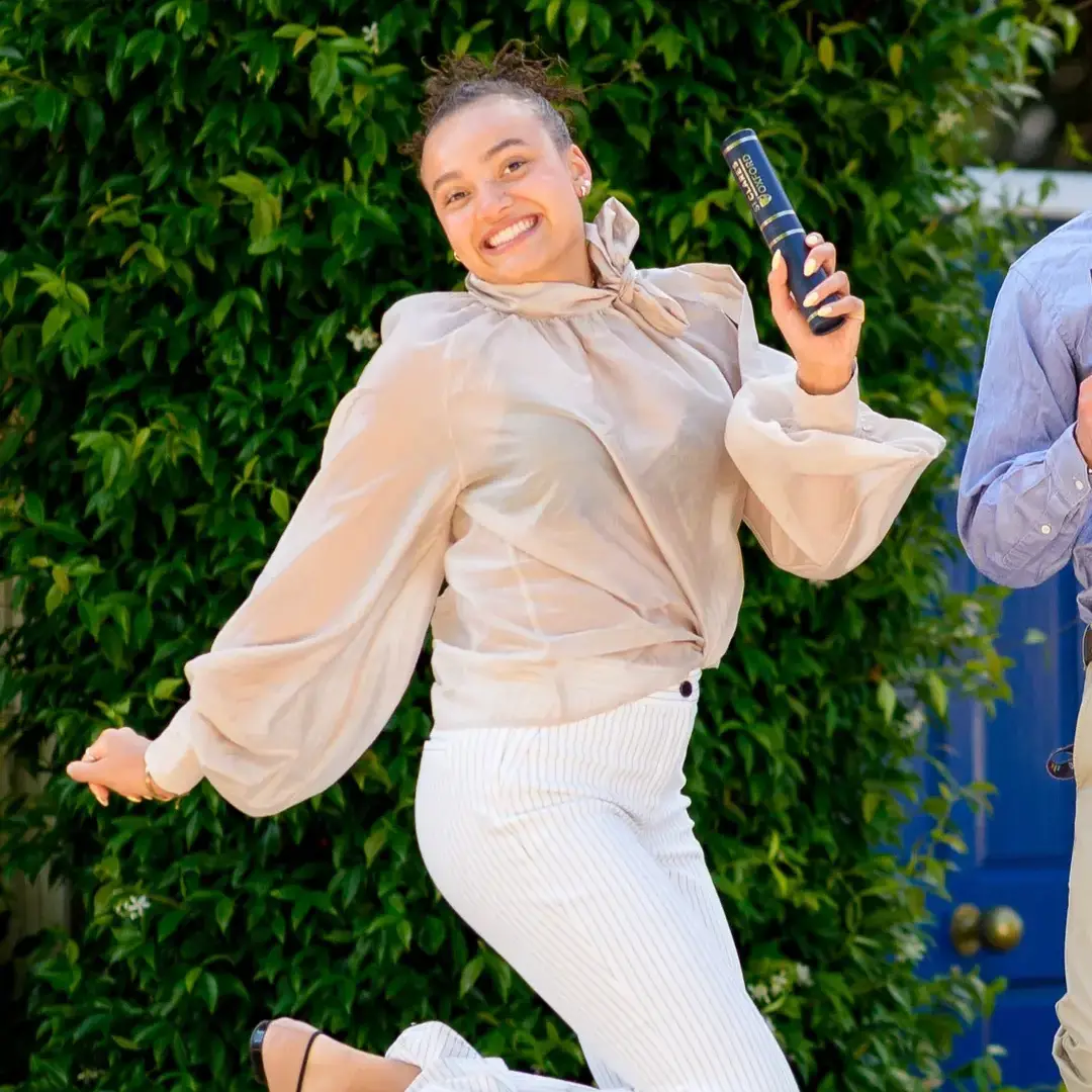 Female student jumping with joy holding graduation tube