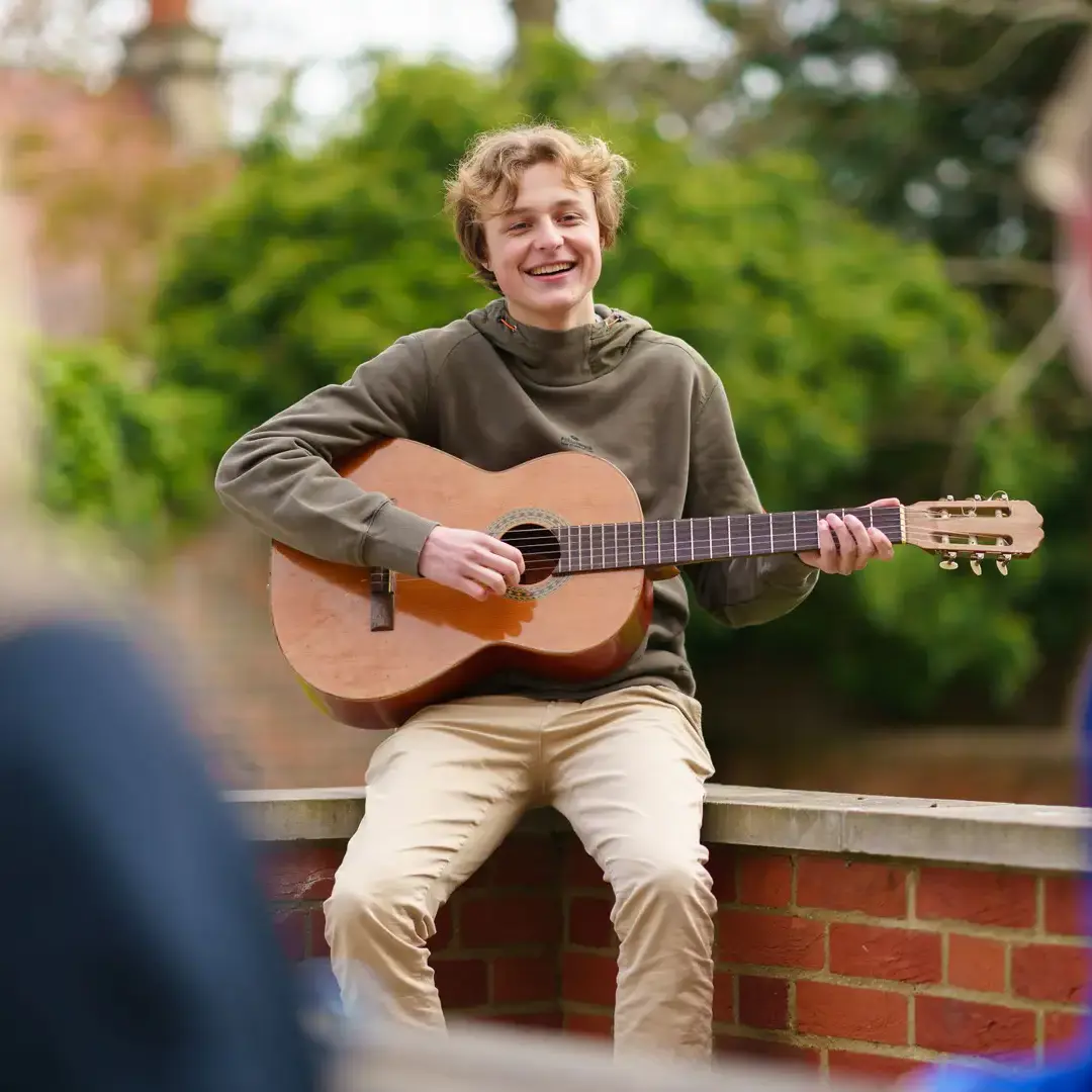 Male student sat in garden playing guitar