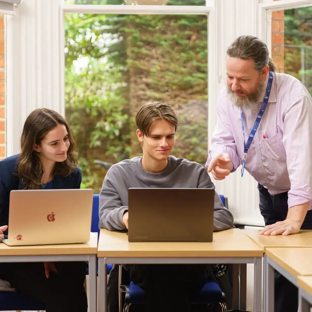 Teacher looking down at students as they work on laptops
