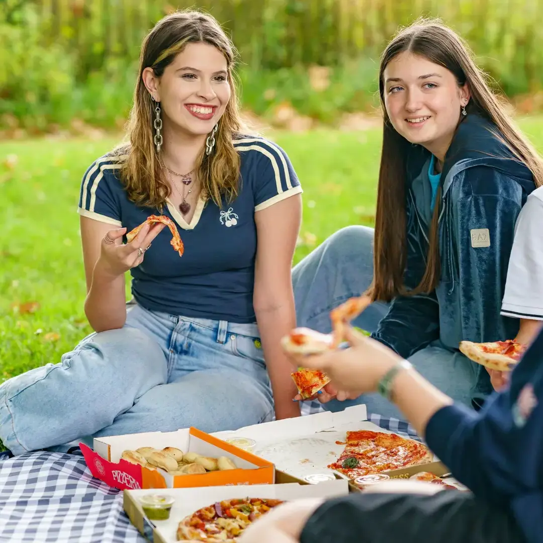 Students eating pizza at picnic and smiling