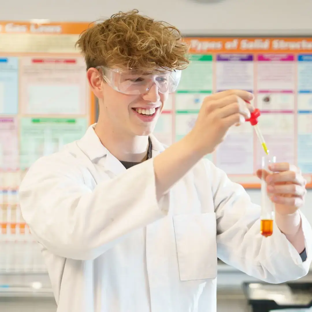 Male student in lab coat doing a Chemistry experiment