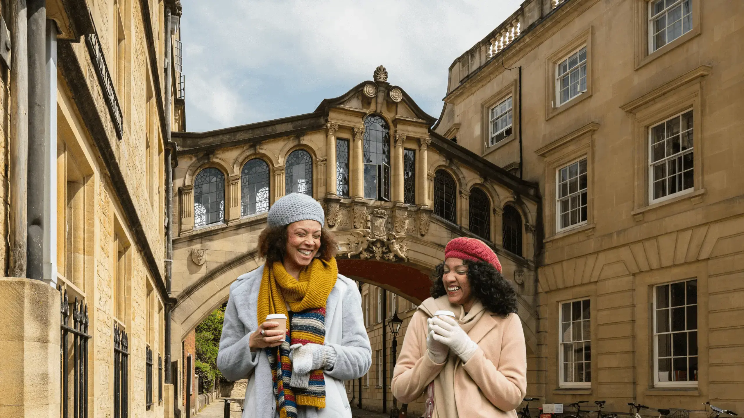 Two teachers walking through Georgian street, holding hot drinks in takeaway cups