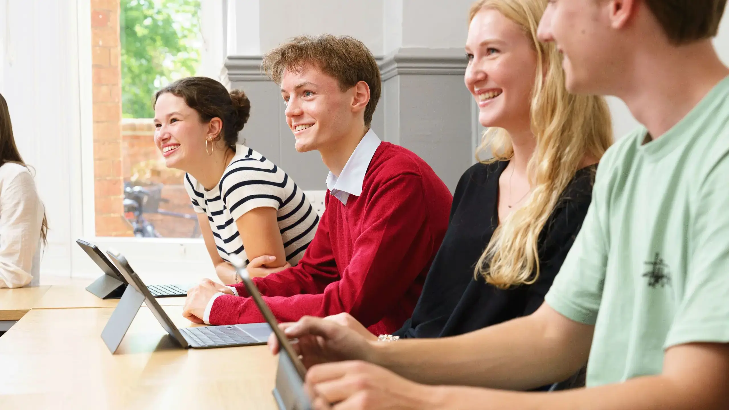 Four students sitting at a desk, smiling up from their work