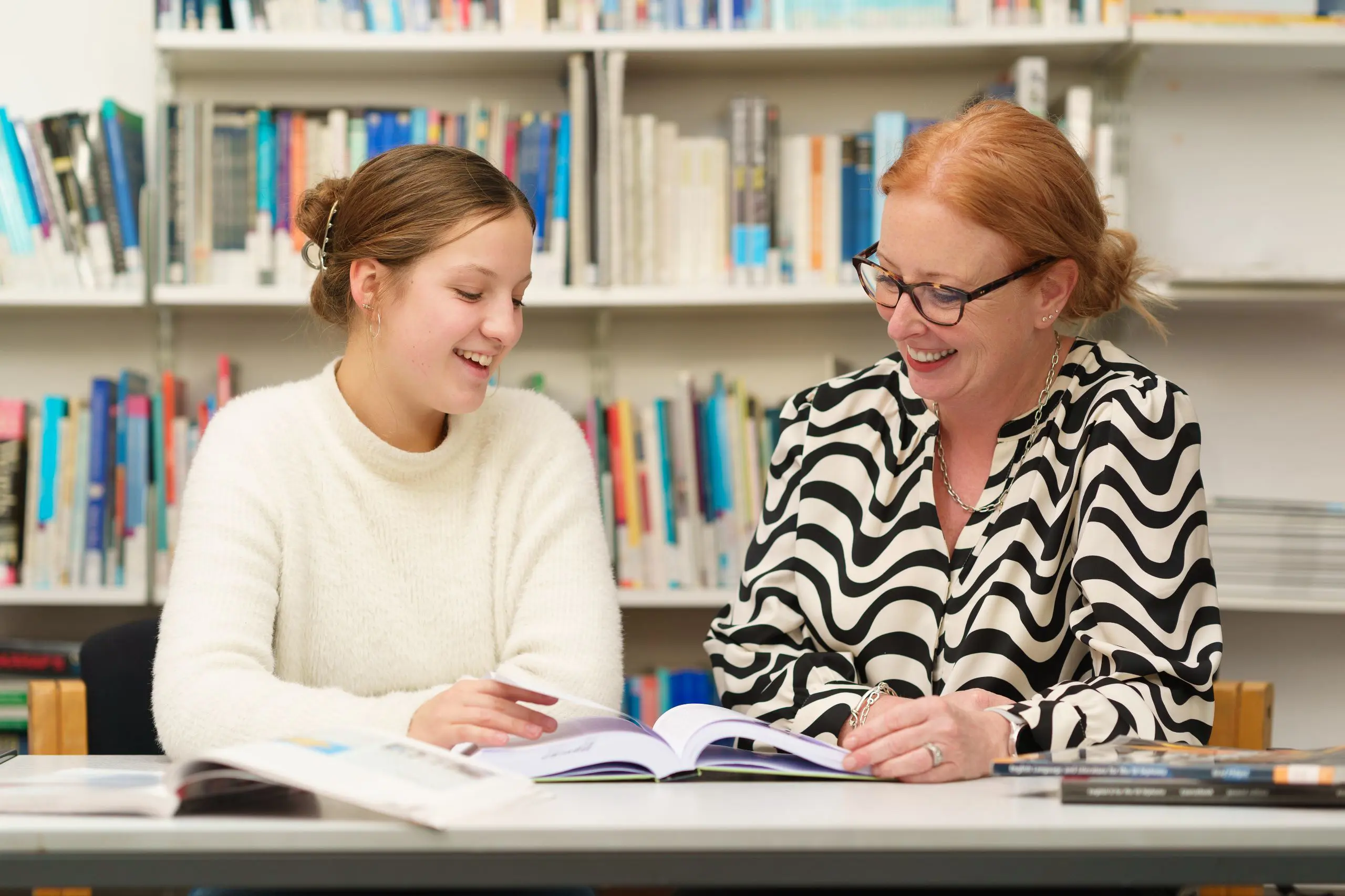 Student and staff member flipping through textbook in library